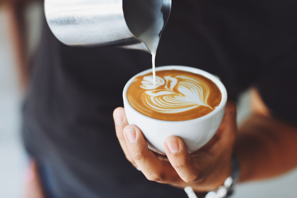 A barista pouring milk into a latte